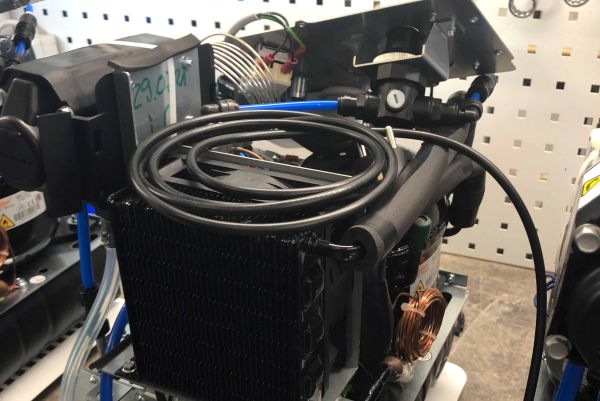 An industrial cooling unit with a black radiator and coiled tubing is set up indoors.