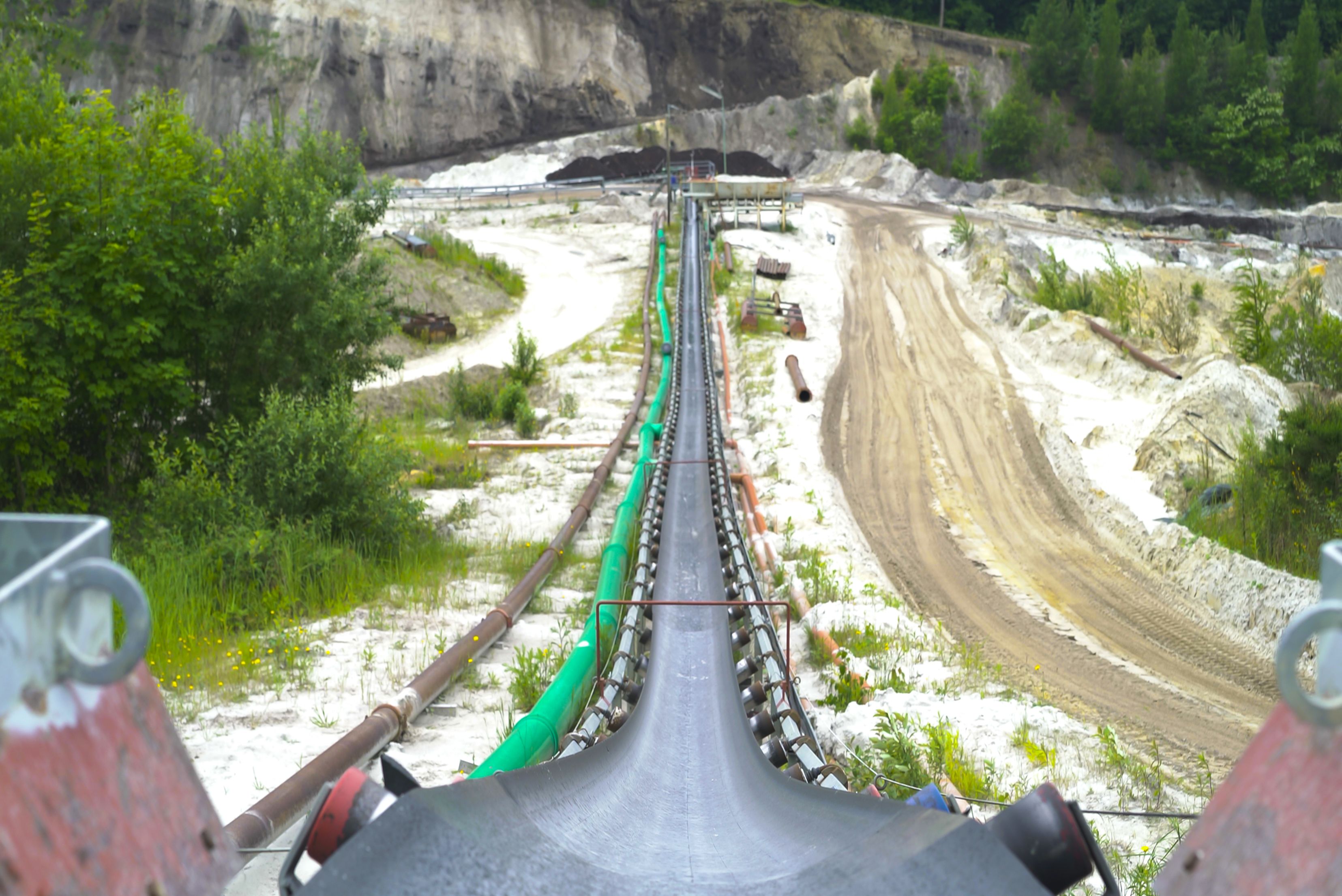 A wide-angle, prospective view along a long overland conveyor belt system running through an open-pit quarry, leading toward excavation walls in the background.
