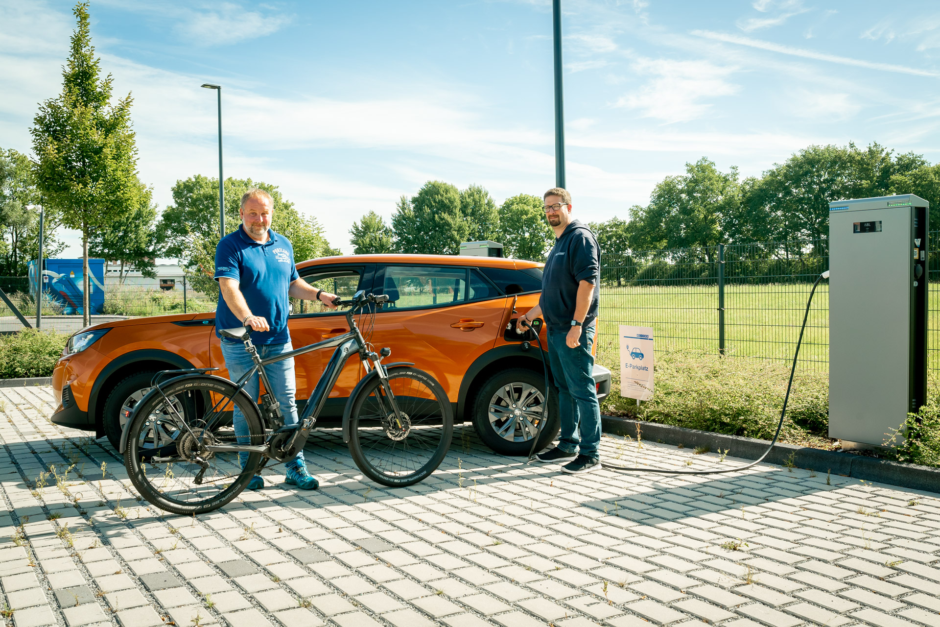 e-mobilitaet-fahrrad-leasing-weicon Zwei MƤnner stehen vor einem E-Auto und laden es auf, der linke hƤlt ein Fahrrad in der Hand