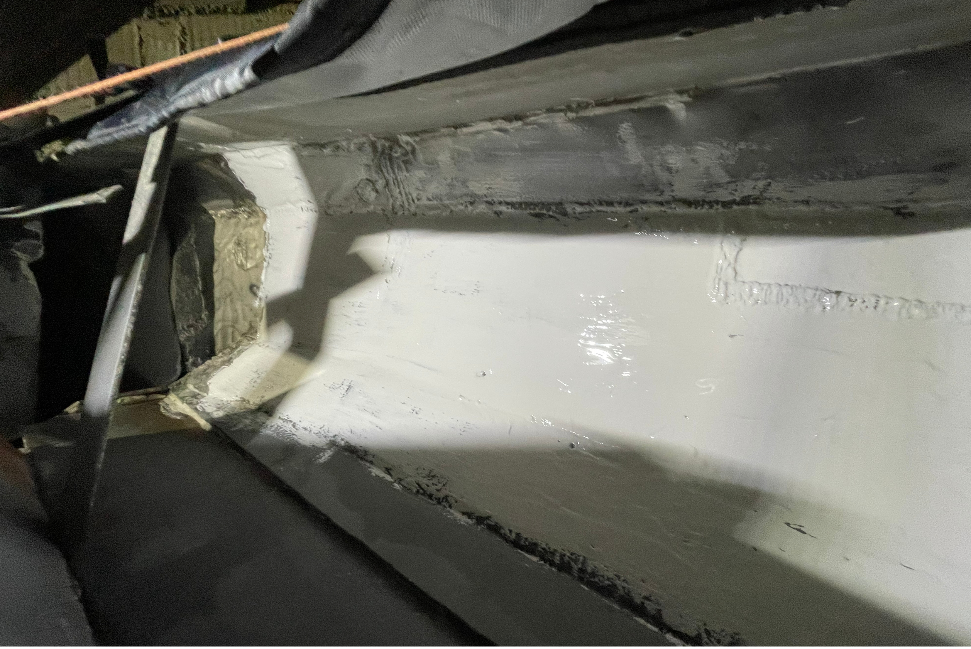 An interior view of a long metal trough or channel featuring a freshly applied, smooth white protective coating along its bottom and lower sidewalls.